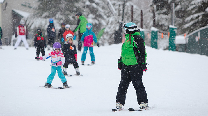 Ski instructor leading group of kids down hill