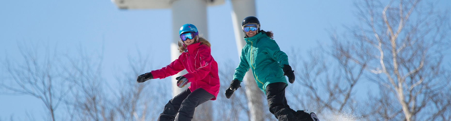Two smiling skiers or snowboarders on a snowy slope, with a woman in a pink jacket and a man in a teal jacket. They are featured on the website's banner for season passes.