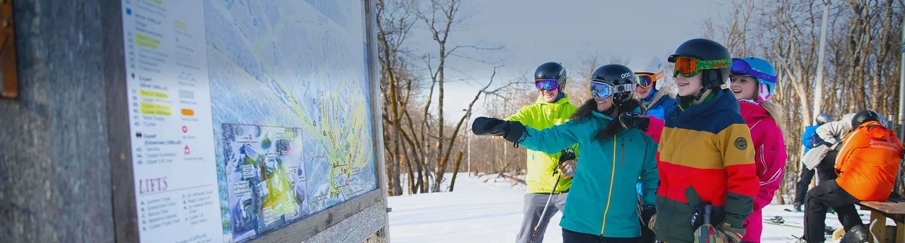 Group of skiers and riders looking at trail map sign